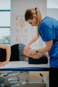 An osteopath in a blue shirt examining a patient's knee while the patient lies on a treatment table.