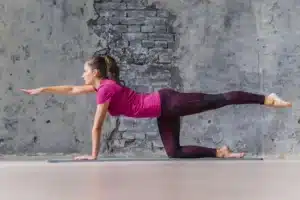 Woman executing a bird-dog pose on a yoga mat to show core stability physiotherapy exercises for lower back pain.