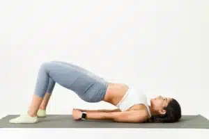 Woman doing a glute bridge exercise on a yoga mat, illustrating strengthening physiotherapy exercises for lower back pain.