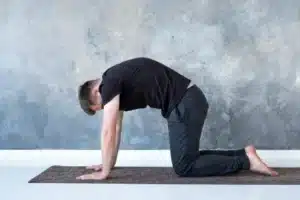 Man performing a cat-cow spinal stretch on a mat to showcase mobility physiotherapy exercises for lower back pain.