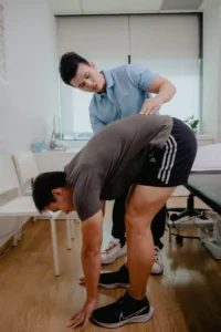 Physiotherapist guiding a patient through standing forward bend movement as part of targeted physiotherapy exercises for lower back pain.