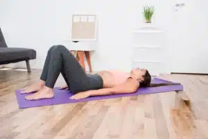 Woman practicing a supine pelvic tilt, demonstrating gentle physiotherapy exercises for lower back pain management.